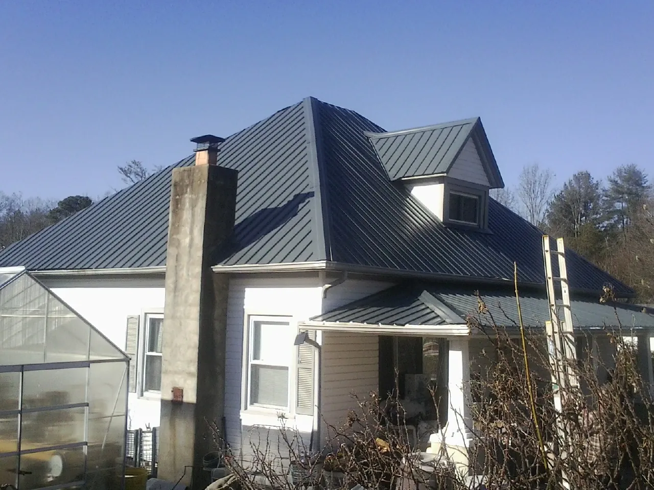 Dark blue standing seam metal roof on a white farmhouse with dormer — Slate & Tile Roof Repair by Roofing Brothers in Riddle