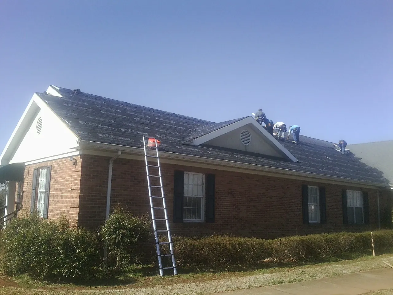Crew tearing shingles off a brick ranch roof with a ladder set — Metal Roof Repair work by our crew in Riddle