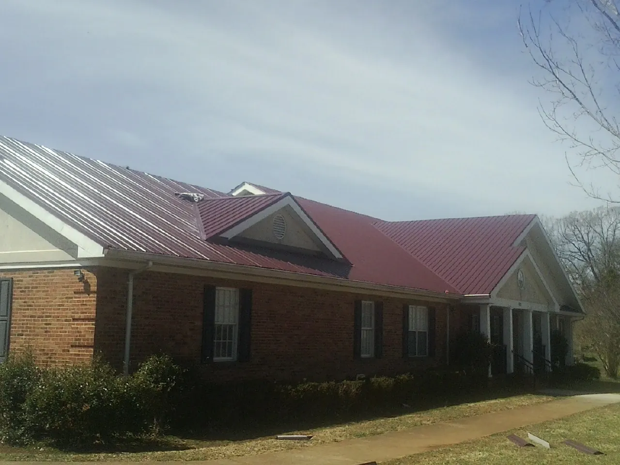 Red metal roof with gabled entries on a long brick building, from a Hail Damage Roof Repair job in Riddle