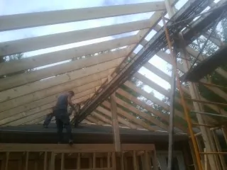 Rafters going up over a new addition with a worker on the wall in Riddle