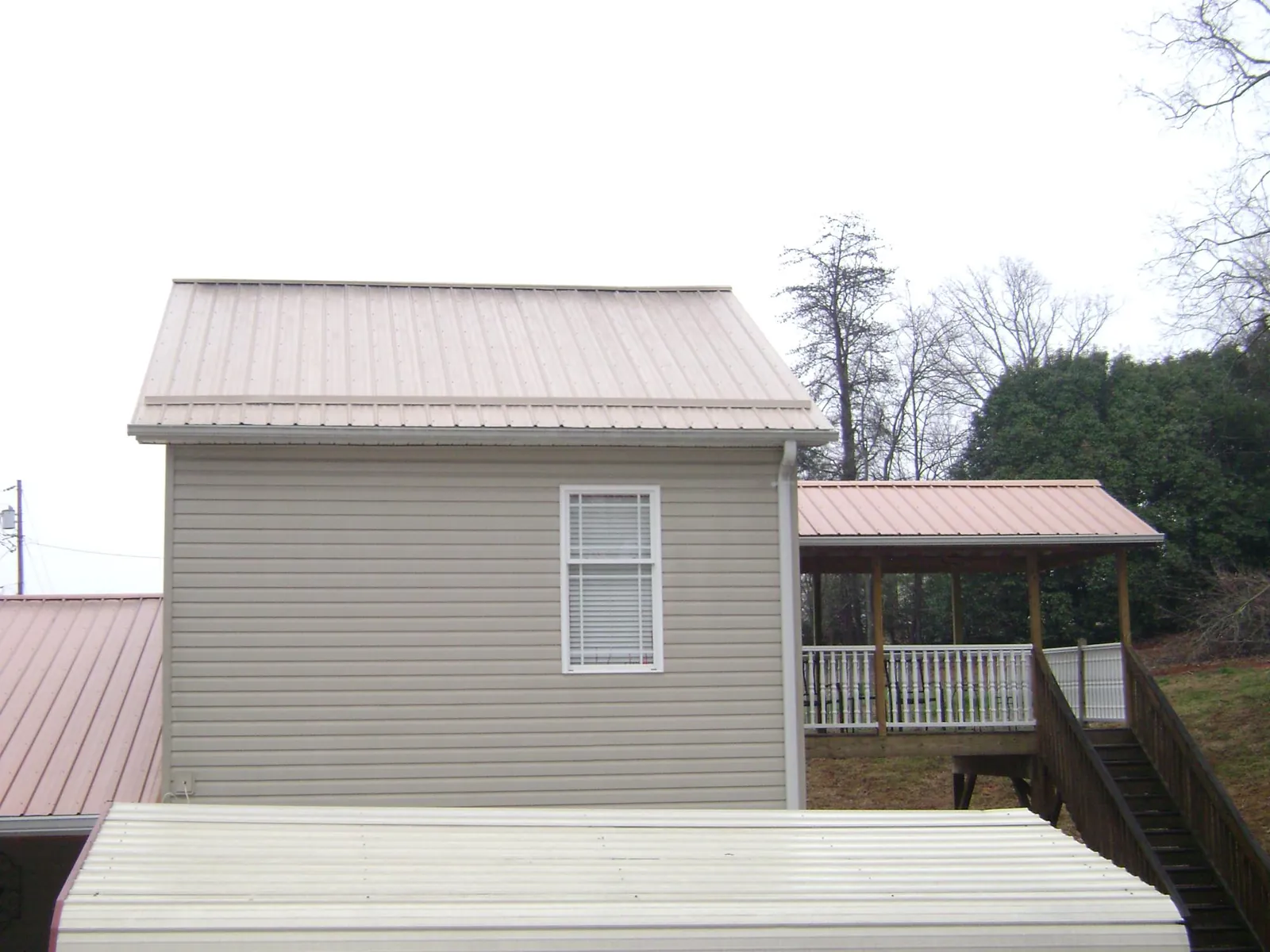 Tan metal roofs on a two story addition and attached porch, from a Roof Replacement job in Riddle